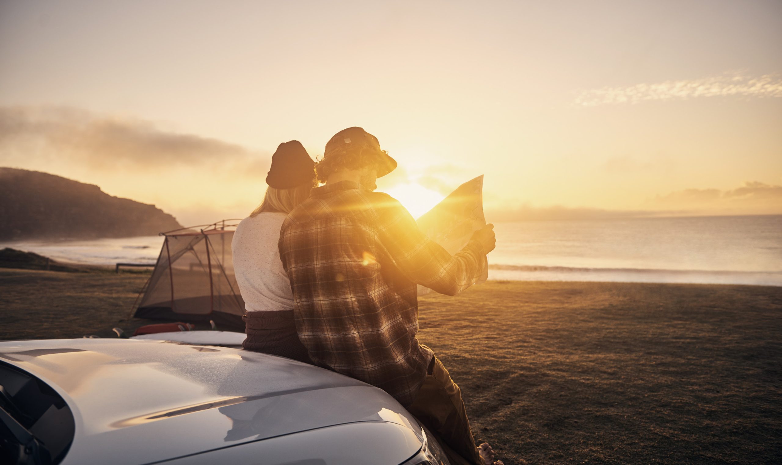 A couple with the sun setting in front of them as they search a map about where to go on their Australian road trip